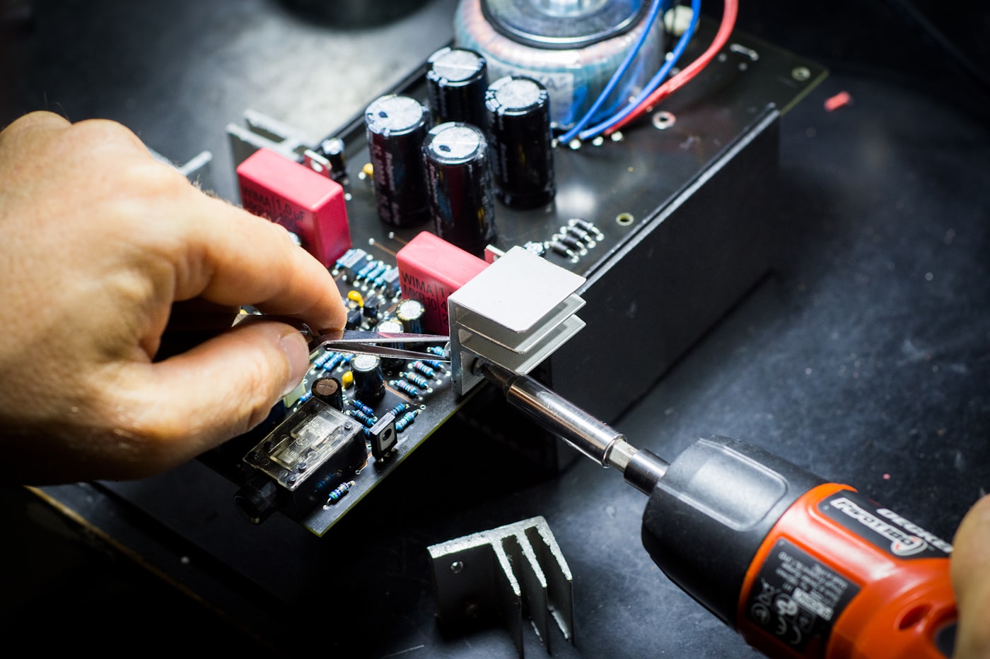 A hand soldering an open circuit board at the Globe Electronics repair bench